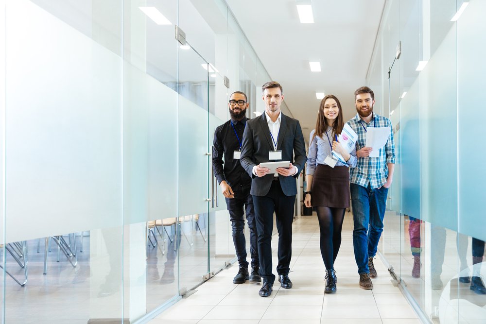 Full-length-of-group-of-happy-young-business-people-walking-the-corridor-in-office-together