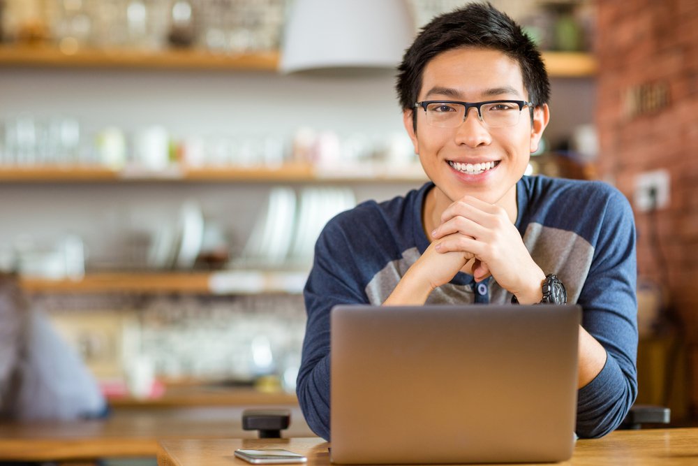 Portrait-of-positive-asian-male-in-glasses-with-laptop-in-cafe