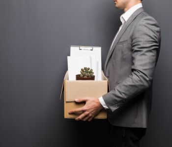 Close up of fired man employee hiding behind box with personal items on grey background