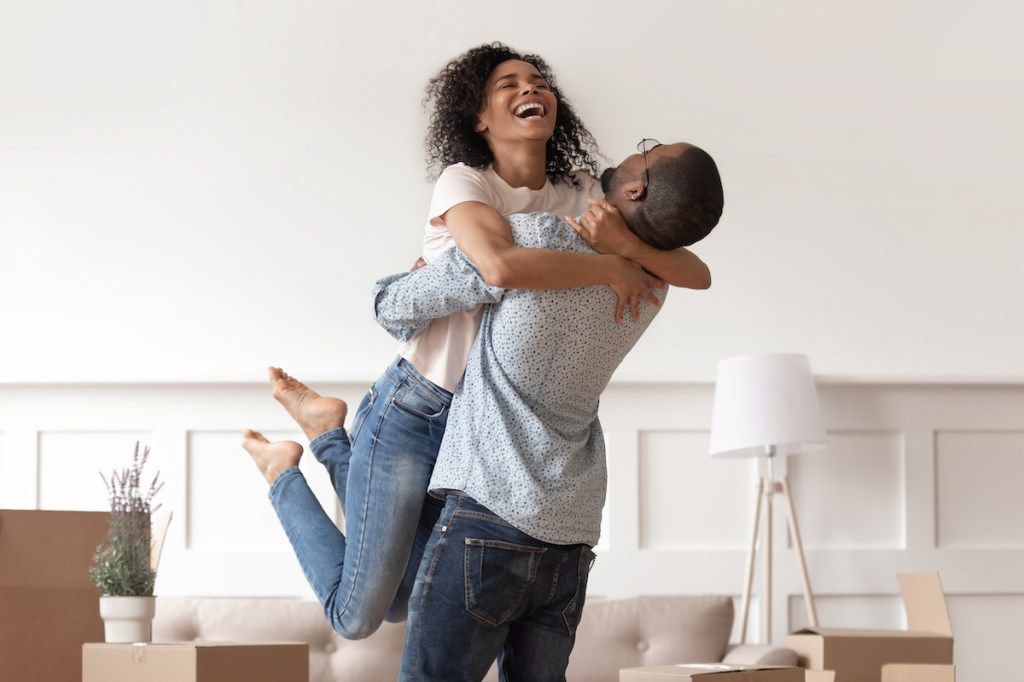 Husband lifting happy wife celebrating moving day with boxes