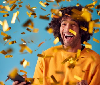 Celebrating Young Man With Mobile Phone Winning Prize And Showered With Gold Confetti In Studio